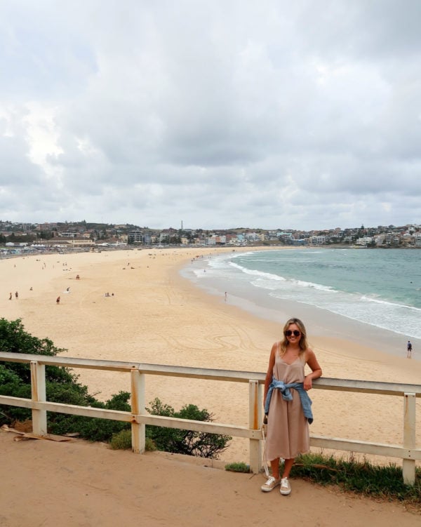 Jessica Sturdy wearing a tan jumpsuit and tied denim jacket with sneakers in Bondi Beach Australia