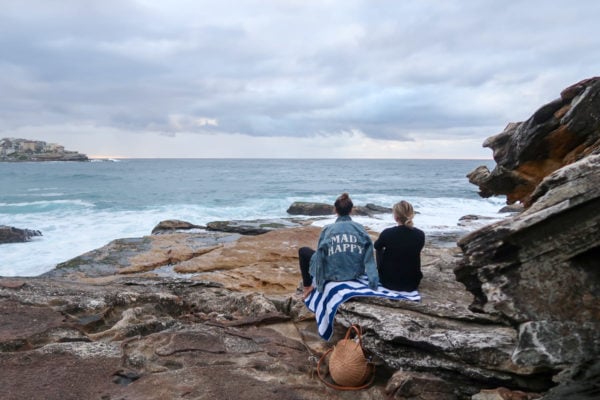 Hallie Wilson and Jessica Sturdy on a rock waiting for sunset in Bondi Beach Australia. Hallie is wearing a Mad Happy jean jacket.