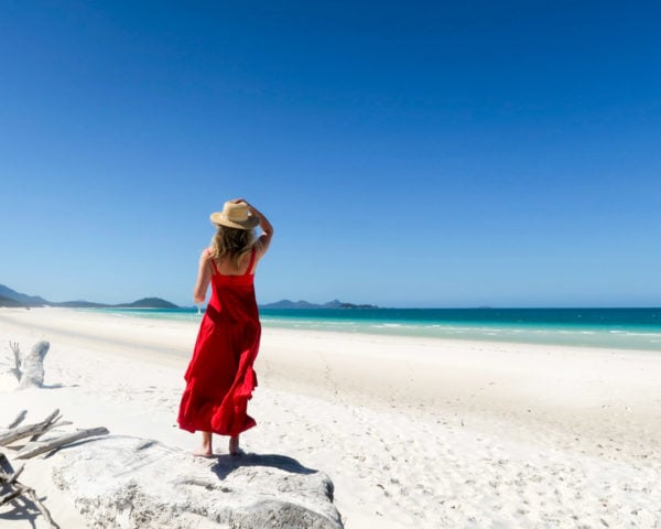Jessica Sturdy on Whitehaven Beach in the Whitsundays in Australia wearing a red maxi dress and a straw hat.