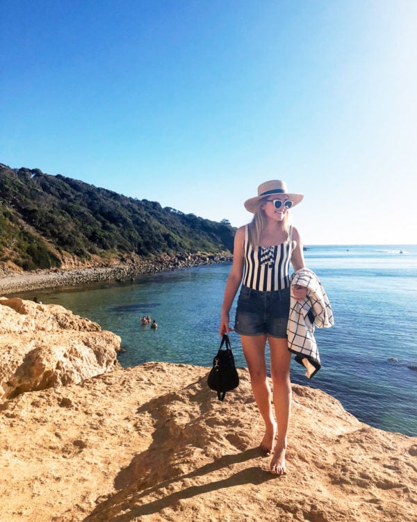 Jessica Sturdy wearing a J.Crew striped swimsuit with jean shorts on a rock cliff overlooking the ocean on the Mornington Peninsula outside of Melbourne Australia