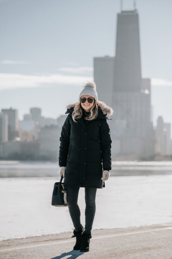 Jessica Sturdy wearing a fur-trimmed, hooded Canada Goose jacket with a pom beanie, matte aviators, booties, and a Polene top handle bag by Lake Michigan.