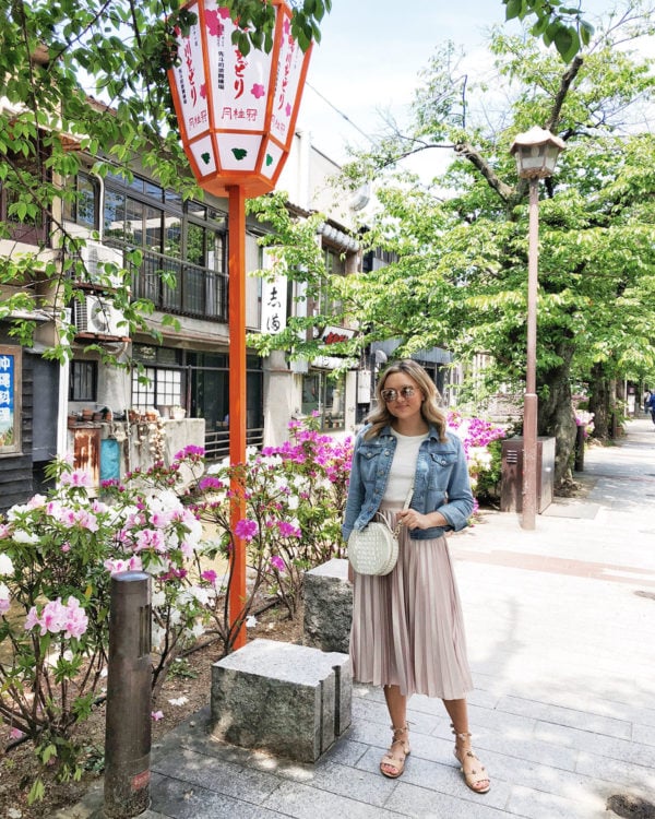 Bows & Sequins Travel Guide in Kyoto Japan. Jessica Sturdy is wearing a denim jacket, pink pleated midi skirt, a Brahmin circle handbag, and Loeffler Randall Saskia sandals.