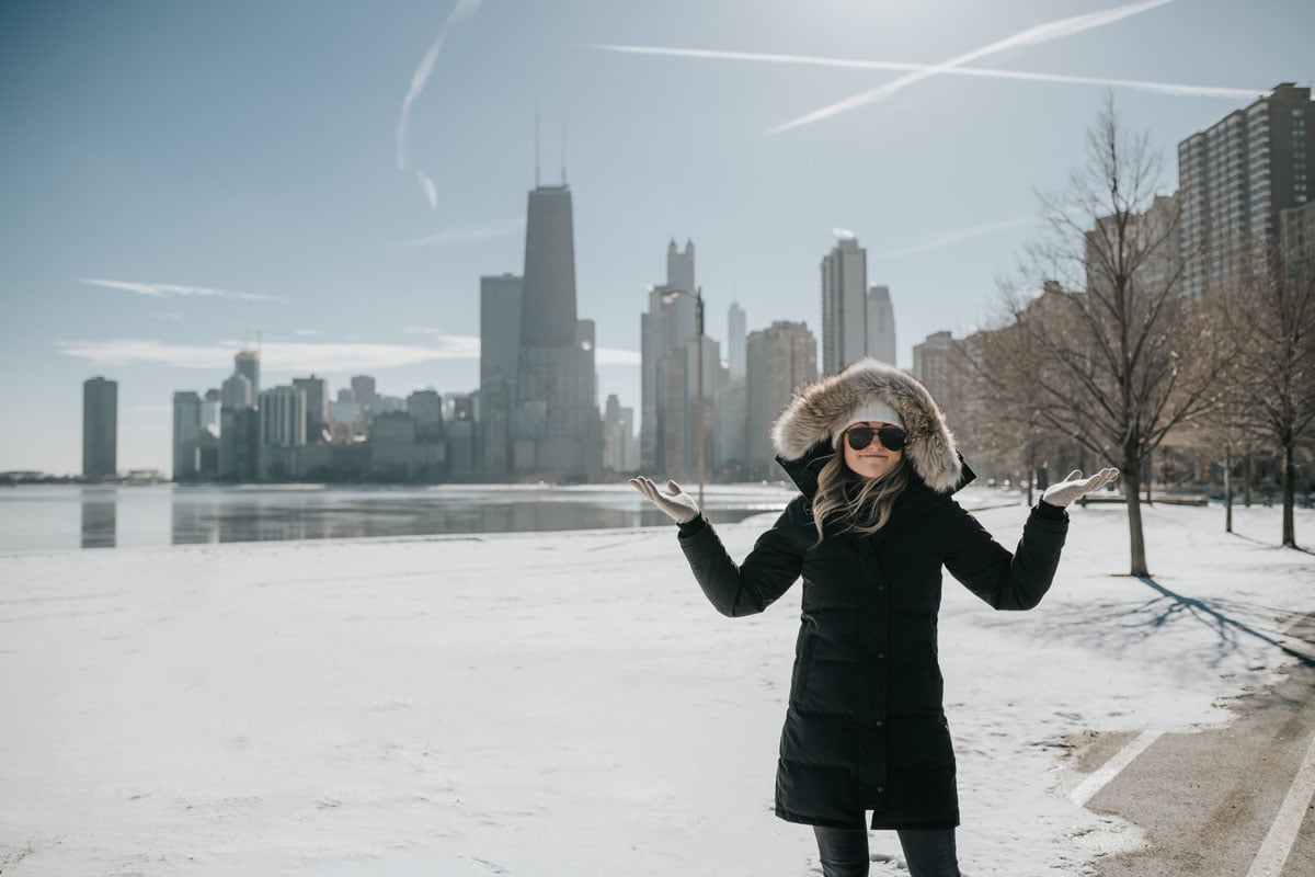 Jessica Sturdy wearing a fur-trimmed, hooded Canada Goose jacket with a pom beanie and matte aviators.