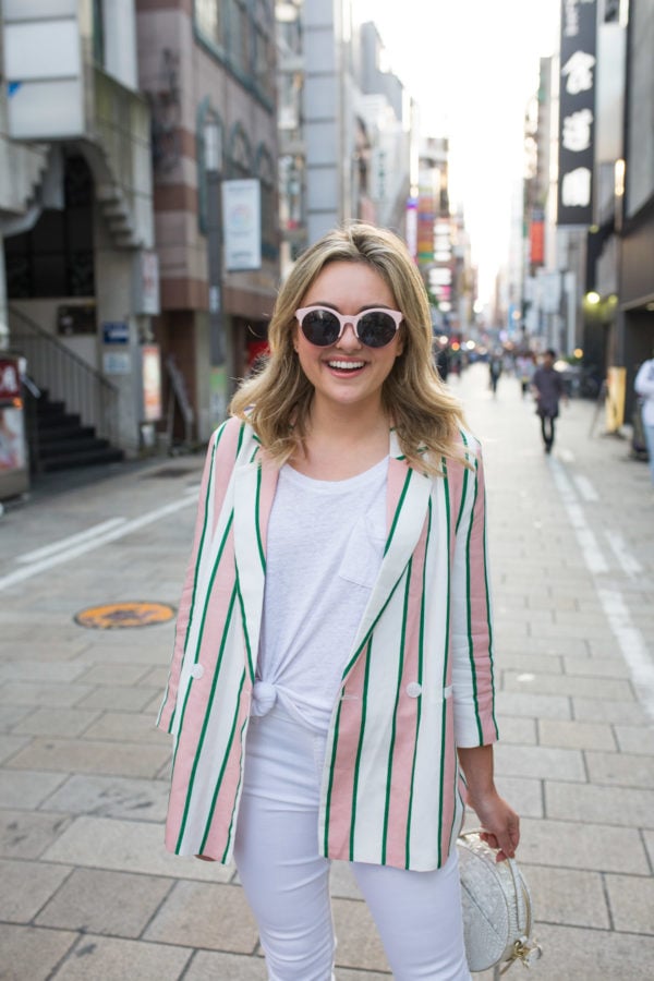 Travel blogger Jessica Sturdy wearing a striped blazer in Japan with pink sunglasses.