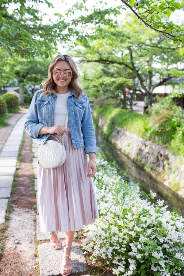 Lifestyle and travel influencer Jessica Sturdy styling a light denim jacket with a white shirt and pleated midi skirt with Loeffler Randall sandals in Kyoto, Japan on Philosopher's Path.