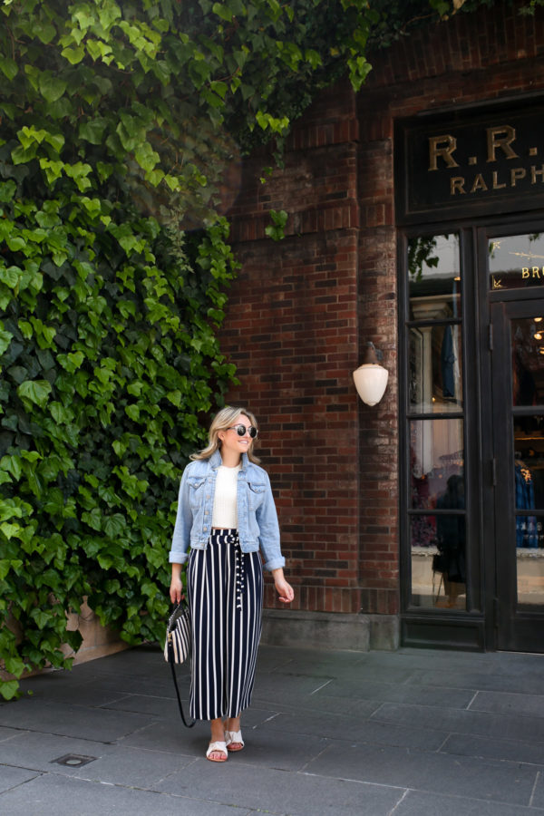 Blogger Jessica Sturdy wearing a denim jacket and striped wide leg pants in front of a green ivy and brick facade in Tokyo.