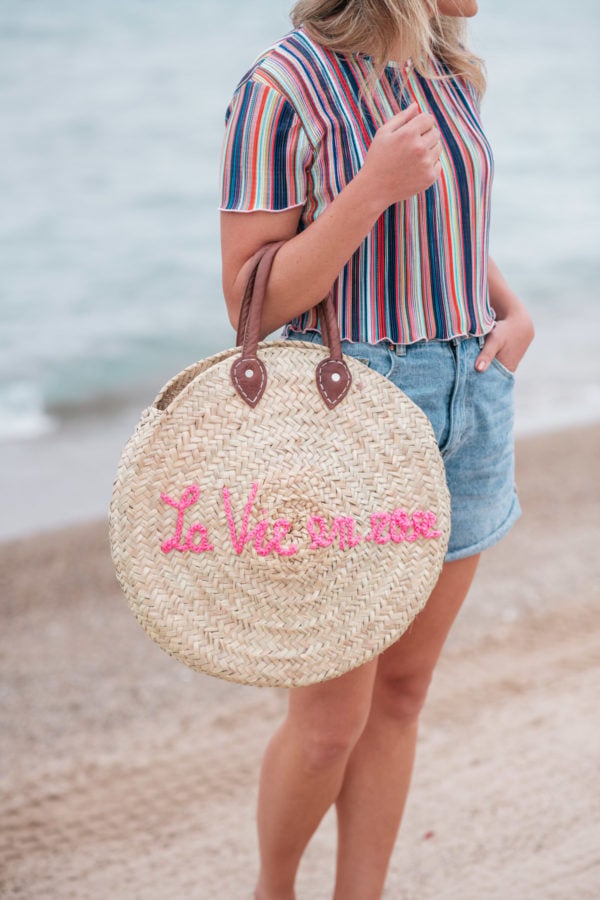 Jessica Sturdy wearing a Bershka striped ruffled hem cropped top with Cotton On high-rise flashback shorts with a "La Vie en Rose" embroidered straw tote created in collaboration with Jessica Sturdy.
