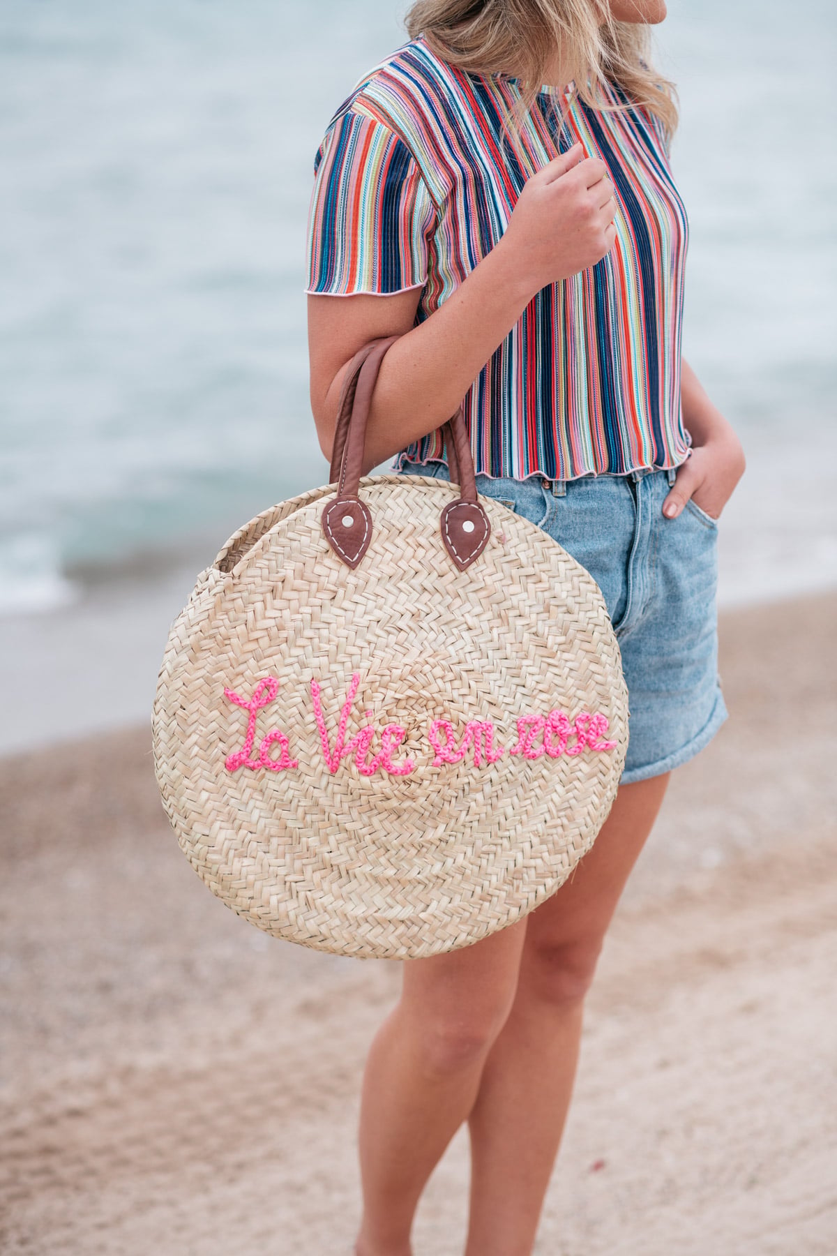 Jessica Sturdy wearing a Bershka striped ruffled hem cropped top with Cotton On high-rise flashback shorts with a "La Vie en Rose" embroidered straw tote created in collaboration with Jessica Sturdy.