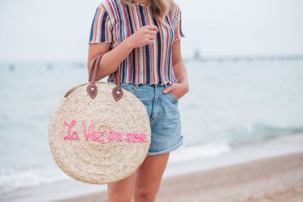 Jessica Sturdy wearing a Bershka striped ruffled hem cropped top with Cotton On high-rise flashback shorts with a "La Vie en Rose" embroidered straw tote created in collaboration with Jessica Sturdy.