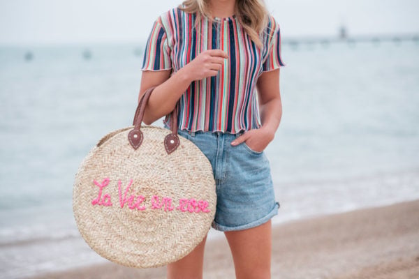 Jessica Sturdy wearing a Bershka striped ruffled hem cropped top with Cotton On high-rise flashback shorts with a "La Vie en Rose" embroidered straw tote created in collaboration with Jessica Sturdy.