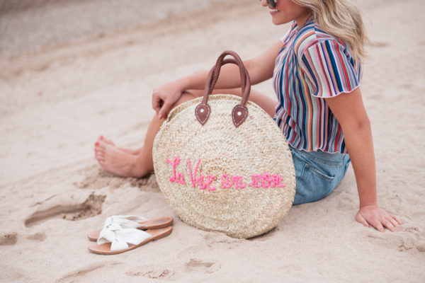 Fashion and lifestyle blogger Bows & Sequins wearing pink sunglasses, a Bershka candy striped short sleeve ruffled hem cropped top and Cotton On high-rise flashback shorts with a White Elephant Designs "La Vie en Rose" embroidered straw tote, designed in collaboration with Jessica Sturdy.