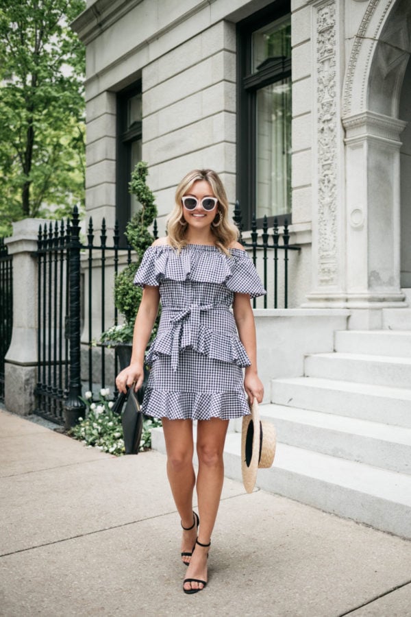Jessica Sturdy wearing a ruffled off the shoulder gingham dress from White Elephant Designs with white and black sunglasses, black block heels, and a straw hat.