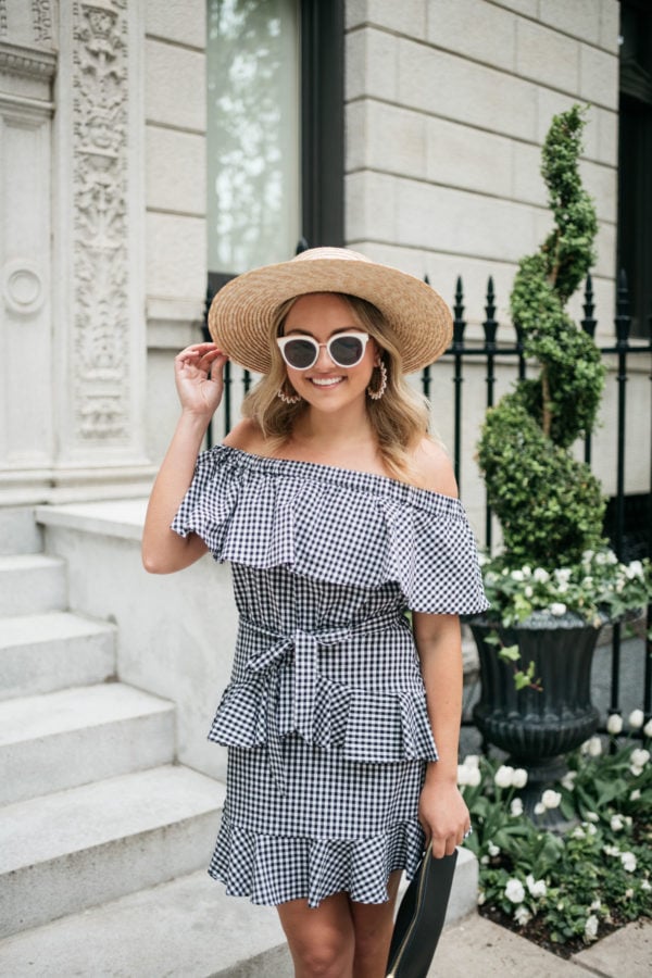 Fashion blogger Jessica Sturdy wearing a straw hat, black and white sunglasses, and an off the shoulder gingham dress with an Old Navy black clutch.