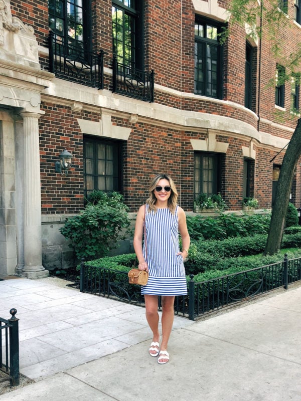 Jessica Sturdy styling a blue and white striped Vineyard Vines dress with white scalloped sandals and a wicker crossbody bag.