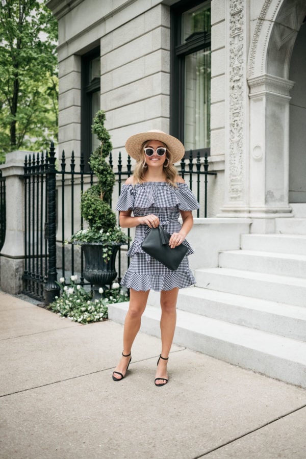 Fashion blogger Jessica Sturdy wearing a straw hat, black and white sunglasses, black block heels, and an off the shoulder gingham dress with an Old Navy black clutch.