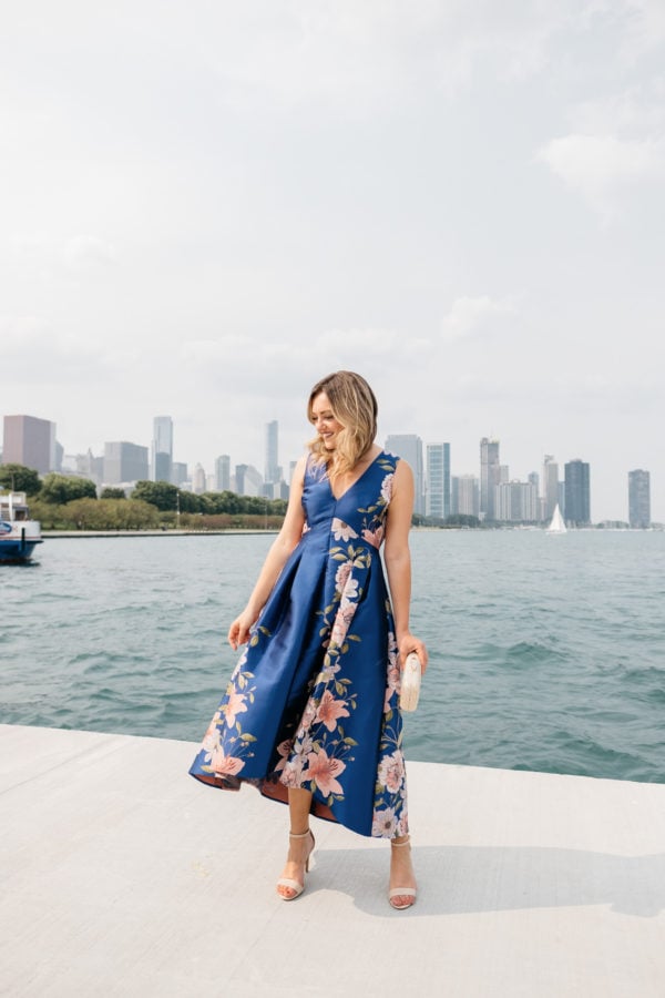 Fashion blogger Jessica Sturdy wearing a pretty blue and pink floral dress by Lake Michigan with the Chicago skyline in the background, one of the best places to take photos in Chicago.