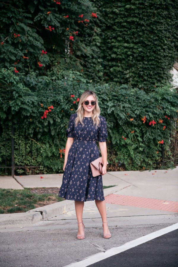 Fashion blogger Jessica Sturdy wearing a floral midi dress with blush pink sandals and a foldover leather clutch.