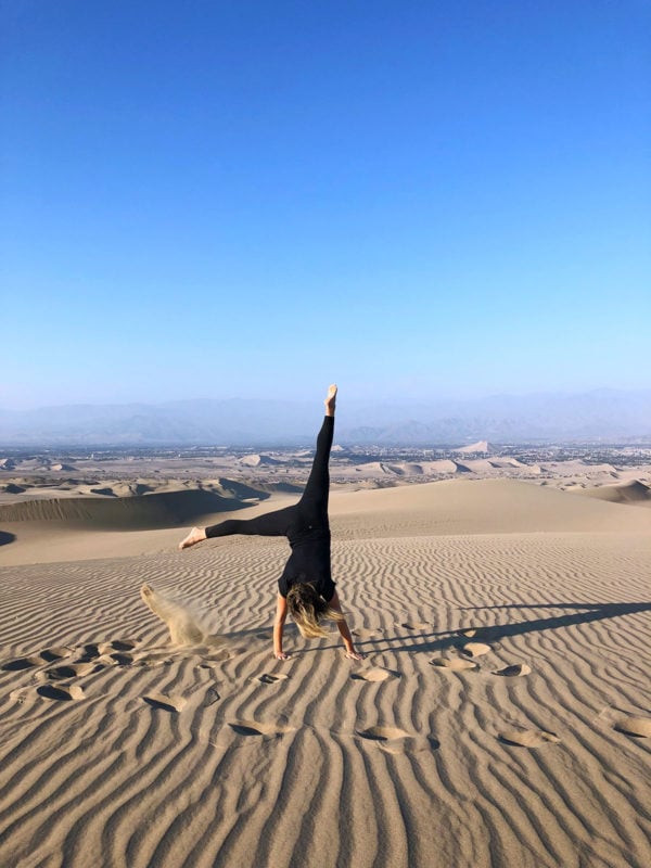 Women's travel blogger Jessica Sturdy of Bows & Sequins doing a cartwheel in the sand dunes of Huacachina in Peru.