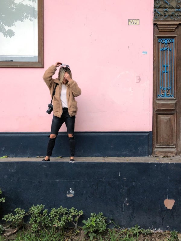 Travel instagrammer Jessica Sturdy of Bows & Sequins in front of a pink and blue wall in Barranco, Lima, Peru. Jessica is wearing a camel teddy coat, sneakers, and black ripped One Teaspoon jeans with a Canon 5D Mark iii. 