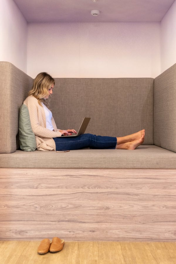 Bows & Sequins sitting on her computer in a nap cubby at Comunal Coworking in Lima, Peru. Her leather slides are on the ground and she's typing on her gold MacBook on her lap, wearing a Sail to Sable cashmere cardigan, white tee by Mott & Bow, and cropped jeans with a raw hem from Old Navy.