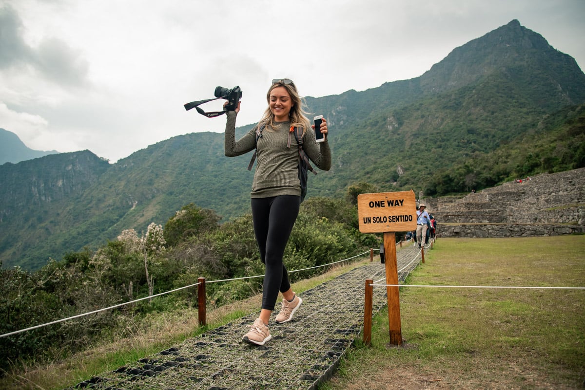 Jessica Sturdy of the travel blog Bows & Sequins at Machu Picchu in Peru on Remote Year Kahlo. Jessica is holding a Canon 5D Mark III camera and wearing a back pack, Lululemon long sleeve tee, black Lululemon leggings, and Adidas UltraBoost sneakers.