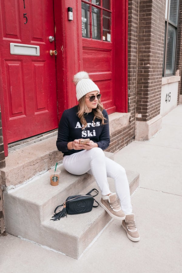 Chicago fashion and lifestyle influencer Jessica Sturdy wearing an Apres Ski sweatshirt with white jeans and shearling and suede sneakers.