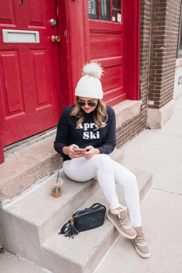 Jessica Sturdy, Chicago-based lifestyle and travel blogger, wearing a Nordstrom 1901 Apres Ski sweatshirt with white jeans while sitting on a stoop in front of a red door.