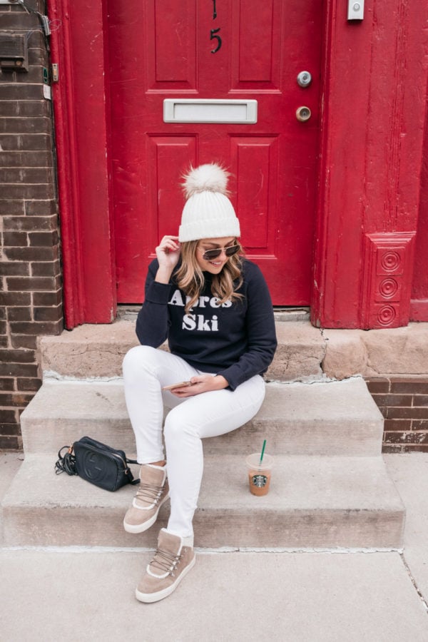Health and wellness blogger Jessica Sturdy sitting on a stoop in front of a red door with an iced coffee and a cute winter weekend outfit.