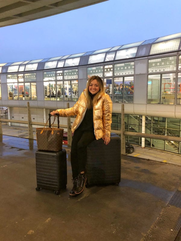 Chicago travel blogger wearing a rose gold puffer coat with black Away suitcases outside of Ohare International Airport.
