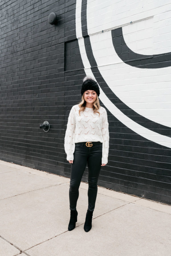 Chicago-based blogger Jessica Sturdy wearing a monochromatic black and white outfit. She's styling a fur beanie with a pointelle balloon-sleeve sweater from Nordstrom, a Gucci belt, leather-like jeans, and black suede ankle booties.