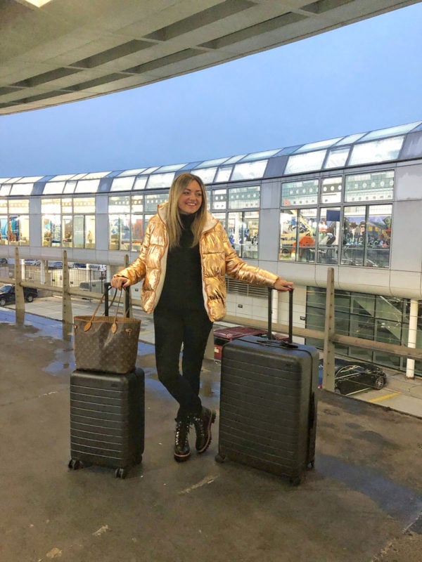 Fashion, travel, and lifestyle influencer Jessica Sturdy at ORD in Chicago wearing a rose gold puffer jacket with an Away Bigger Carry-On and an Away Large suitcase with a Louis Vuitton Neverfull bag.