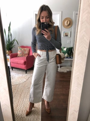 Lifestyle blogger Jessica Sturdy of Bows & Sequins wearing a striped crop top with white wide leg pants, pointed pumps, and a Michael Kors bag.