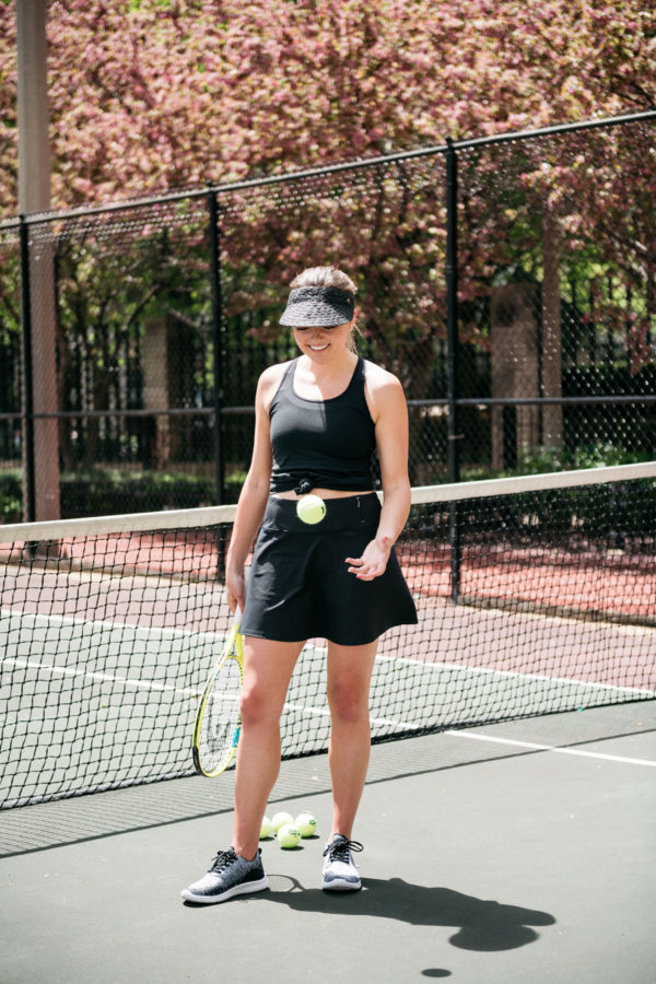 Chicago blogger Bows & Sequins playing tennis in black skort and visor.