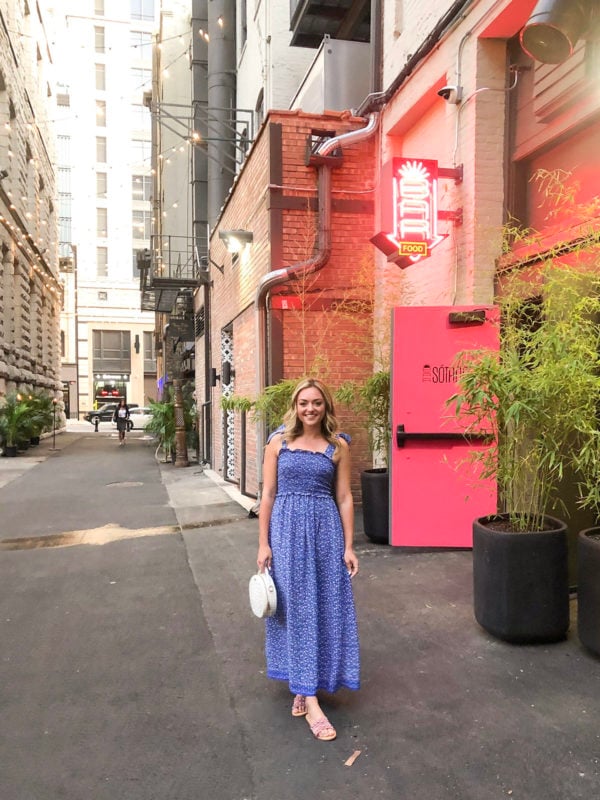 Blue floral smocked maxi dress with tie-shoulder straps and blush pink studded slide sandals outside of Bar Sotano in Chicago