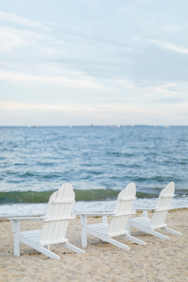 White wooden adirondack chairs on the sand at Wee Burn Beach Club in Connecticut