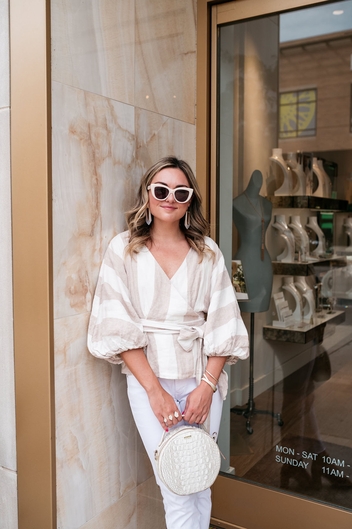 Chicago fashion lifestyle blogger Jessica Sturdy of Bows & Sequins wearing a striped linen top by Mara Hoffman with white denim, cream-colored sunglasses, a round handbag and Kendra Scott mother of pearl jewelry.