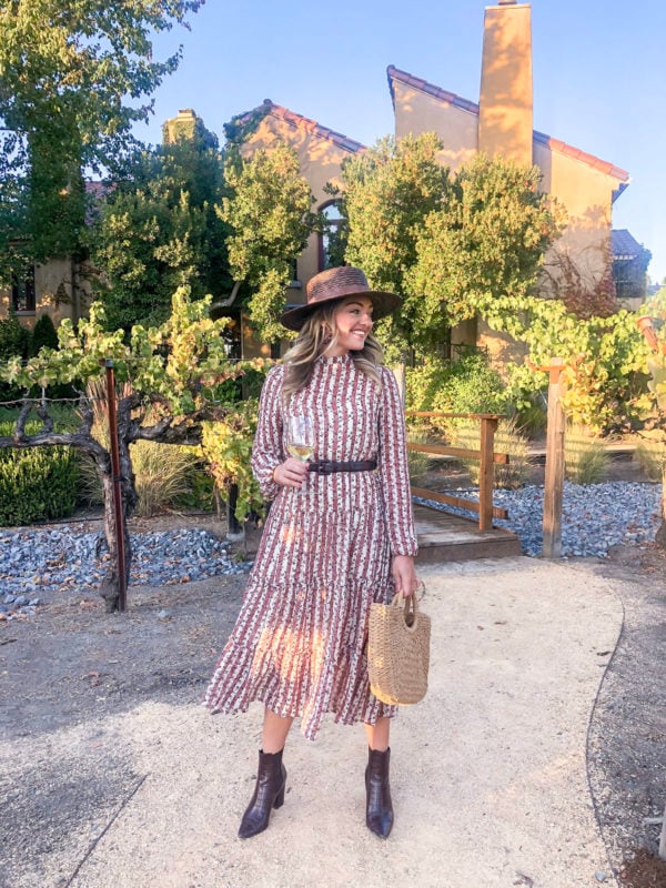 Fashion and travel blogger Jessica Sturdy wearing a long sleeve midi dress with dark brown croc boots, a brown waist belt, and a dark brown straw hat in the vineyard at Vintners Inn Resort for dinner.