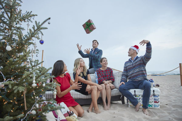 Dave Adams throwing a Christmas present in the air to John Philp Thompson while Jessica Sturdy and Liz Adams are on the couch on the beach.