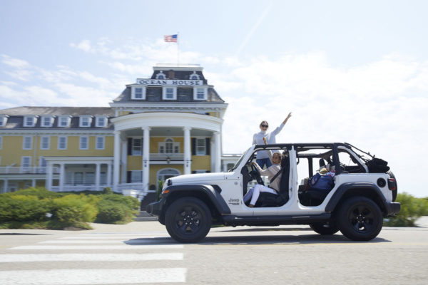 Caila Quinn driving a white Jeep with Jessica Sturdy standing out of the sunroof in front of Ocean House in Watch Hill, Rhode Island.