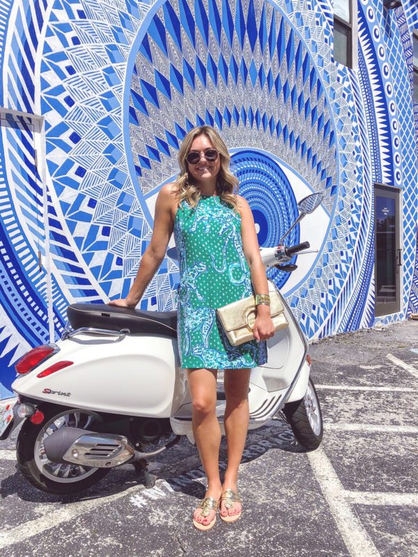 Jessica Sturdy wearing Lilly Pulitzer in Palm Beach in front of a white Vespa and blue and white printed wall mural.