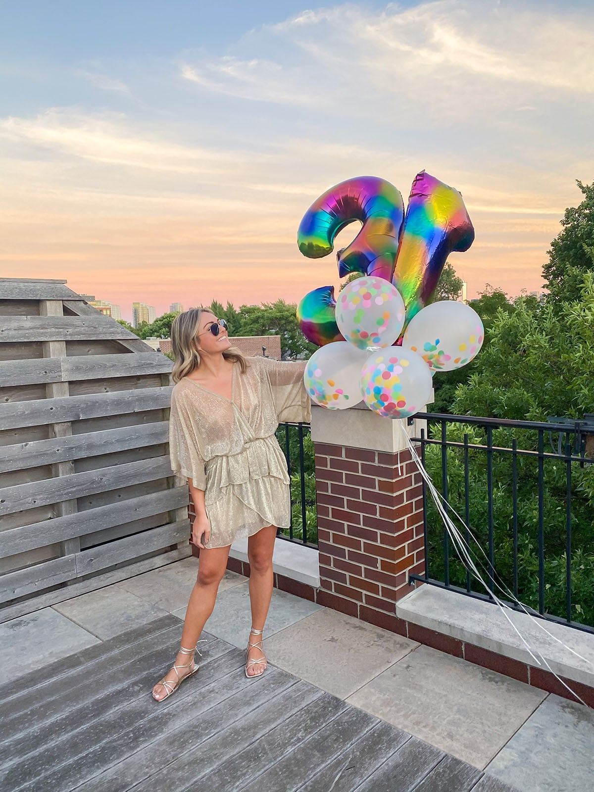 Jessica Sturdy at her Golden Birthday Party wearing a sheer gold sparkly dress by IRO, metallic lace-up sandals by Marc Fisher, and holding rainbow numbers and confetti filled balloons.