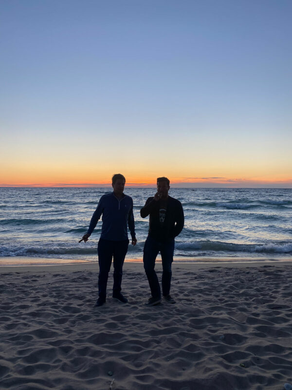 Two guys standing on a beach at sunset smoking cigars