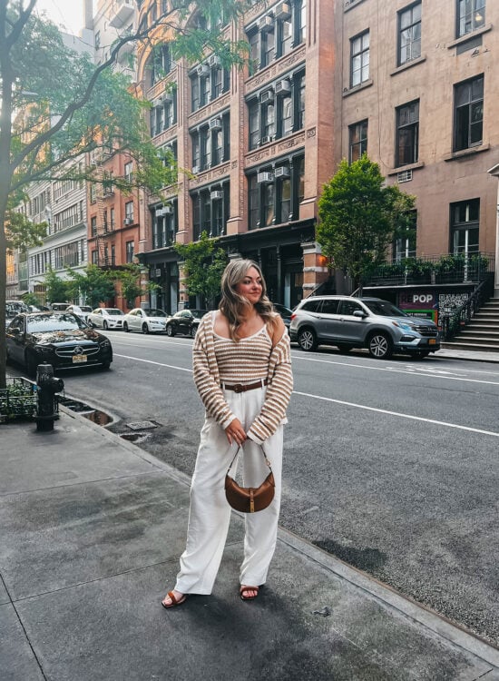Fashion blogger Jessica Sturdy of Bows & Sequins blog wearing white trousers, a striped crochet sweater set, and a Ralph Lauren Polo ID bag in the West Village