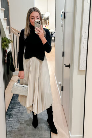 Fashion and style blogger Jessica Sturdy wearing a dressy winter outfit! She has on a J.Crew black turtleneck, Kate Spade oversized bow belt, Ralph Lauren pleated skirt, Stuart Weitzman sock booties, and a silver mini bag.