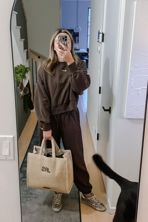 Style blogger wearing a road trip travel outfit. Brown Nike jogger sweatpants and cropped sweatshirt, glitter Golden Goose sneakers, and a monogrammed sherpa Teddy Bear tote by Poolside.