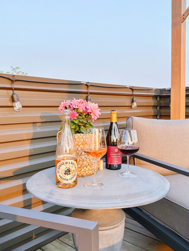 Wellness blogger Jessica Sturdy of Bows & Sequins shares about her sober curiosity and what she's realized from not drinking. Pictured is a bottle of non-alcoholic sparkling rosé next to a bottle of red wine on a patio at sunset.