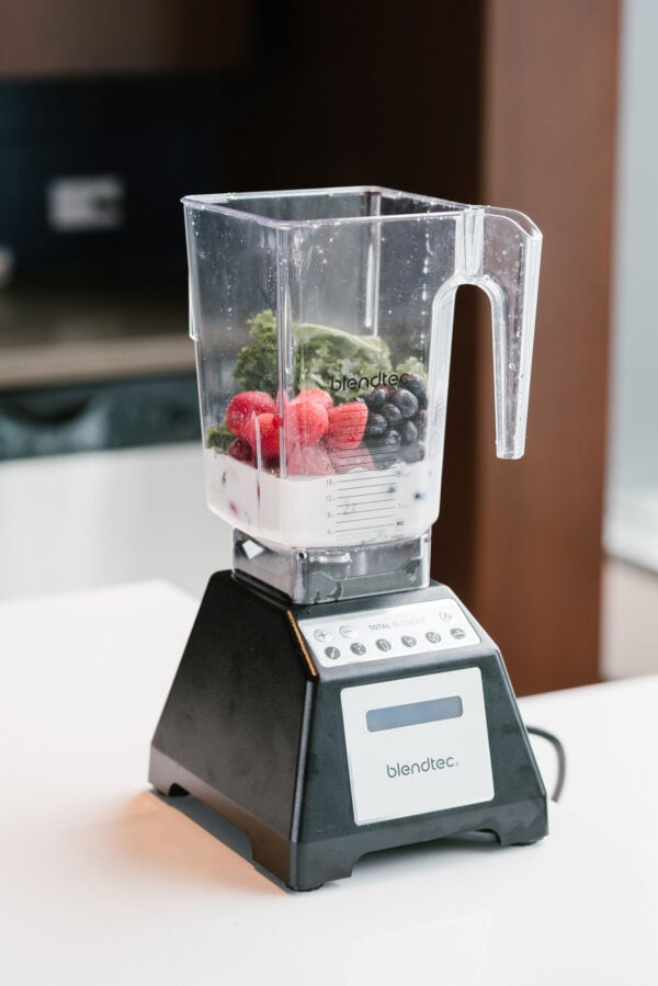 Blendtec Blender with almond milk, strawberries, blueberries, and kale inside.