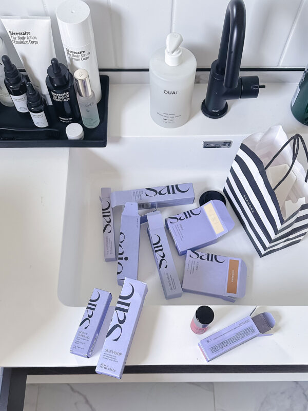 Lilac Saie Beauty boxes open on bathroom counter in front of a Sephora bag. Chicago beauty blogger Bows & Sequins shares her favorite products to buy in the Sephora Spring Sale.