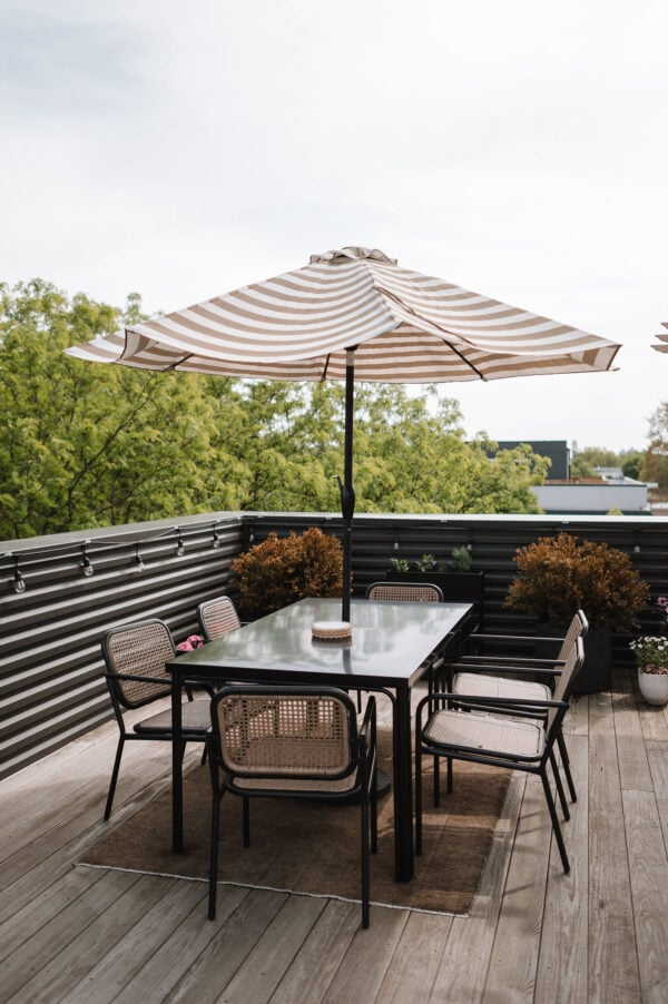 Home decor blogger Bows & Sequins shares a look at her Chicago rooftop space with a chic striped patio umbrella, a modern black aluminum dining table, and woven rattan chairs.