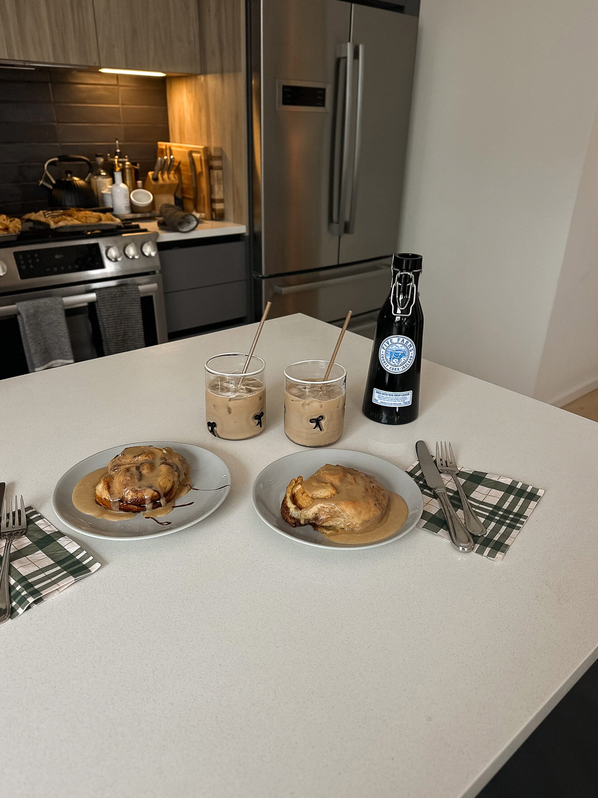 Two homemade cinnamon rolls with icing and iced coffee on a modern kitchen island